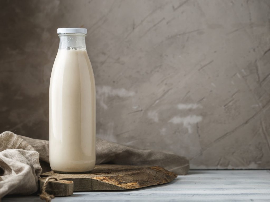 Một chai sữa thuỷ tinh được đặt trên một tấm gỗ, ở bên trái tấm hình