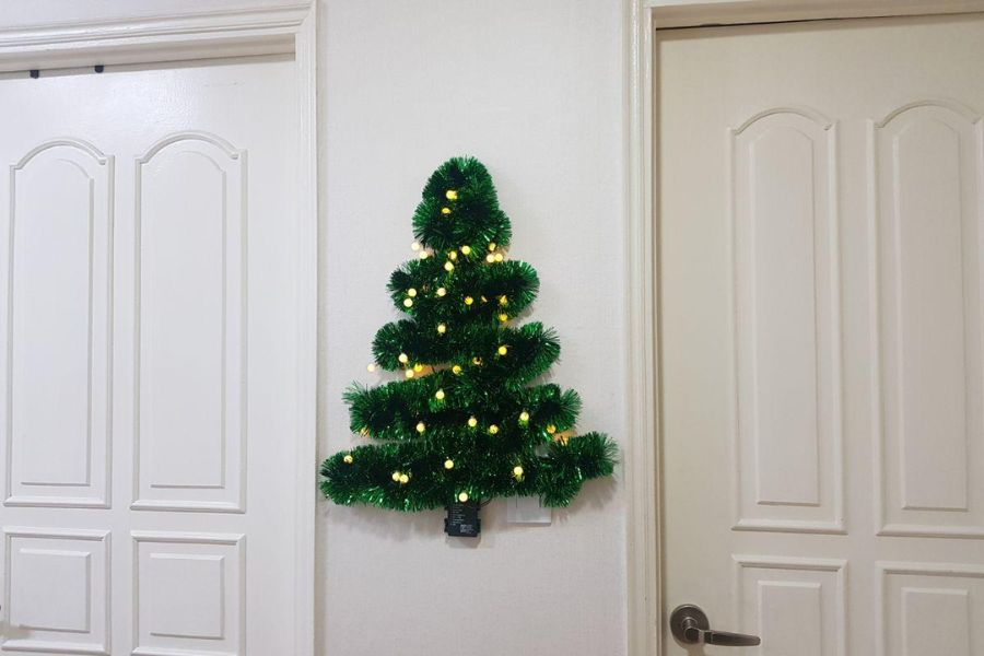 Bạn có thể cố định cây thông Noel ngay trên tường nhà bằng băng keo hoặc đinh.