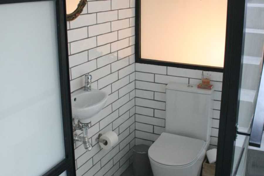 Nhà vệ sinh nhỏ dưới cầu thang được ốp bằng gạch trắng và cửa sổ giả